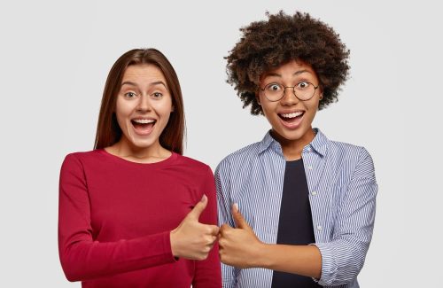 two-women-give-thumbs-each-other-show-their-agreement-smile-gladfully-stand-shoulder-shoulder-white-wall-gesture-indoor-interracial-friends-being-glad-give-okay-sign-feel-overjoyed (1)
